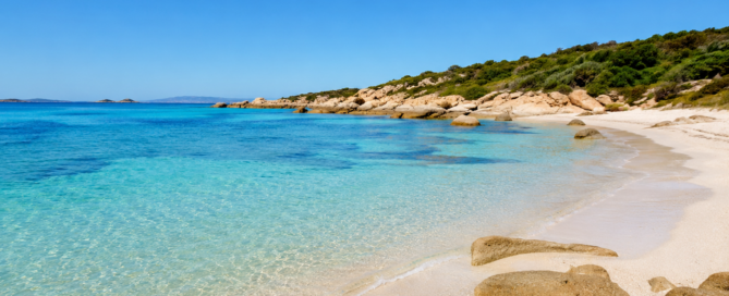 Deserted Mediterranean beach at midday with clear turquoise water, pale sand and granite rocks