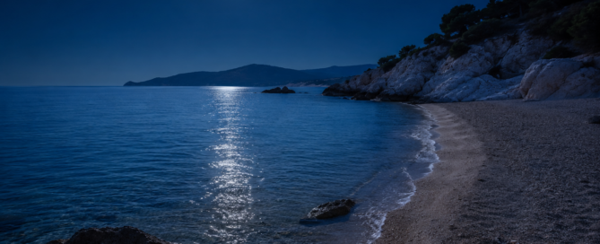 Mediterranean beach at night with a full moon reflecting on the calm sea